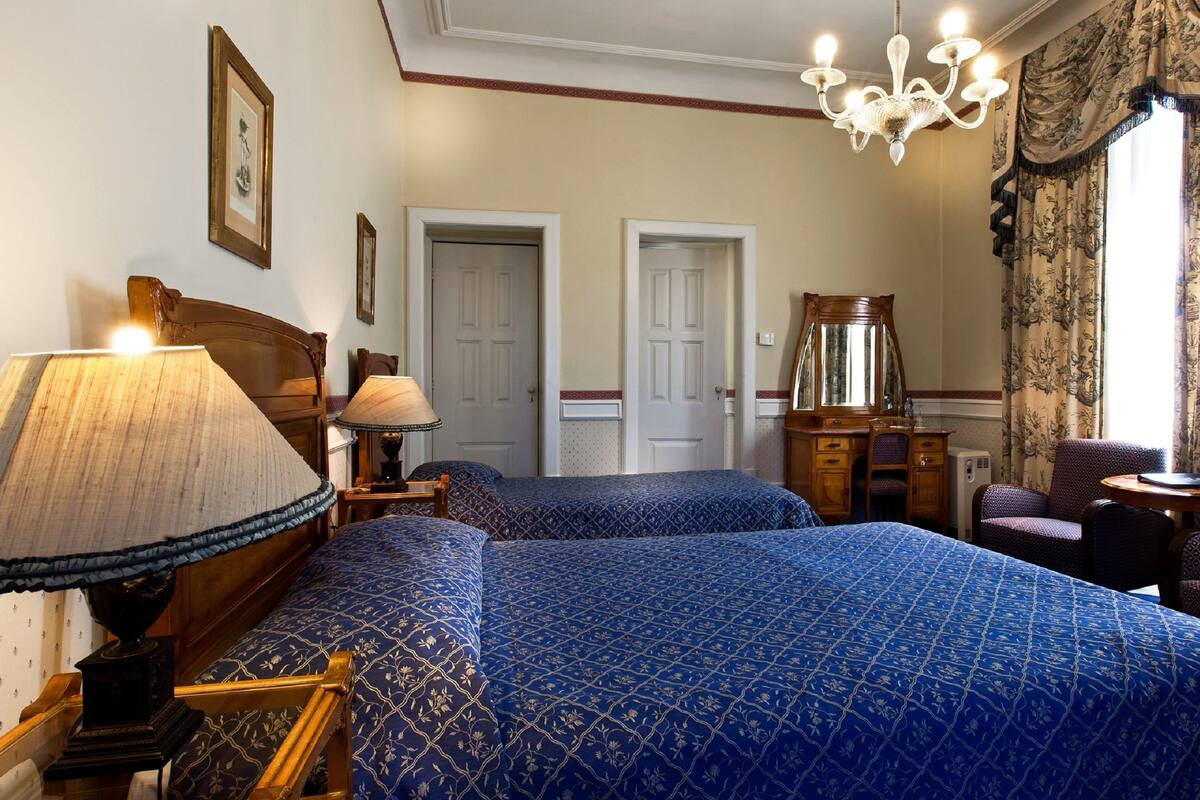 A hotel room with two beds, a desk, a chair, a dresser, and a chandelier.