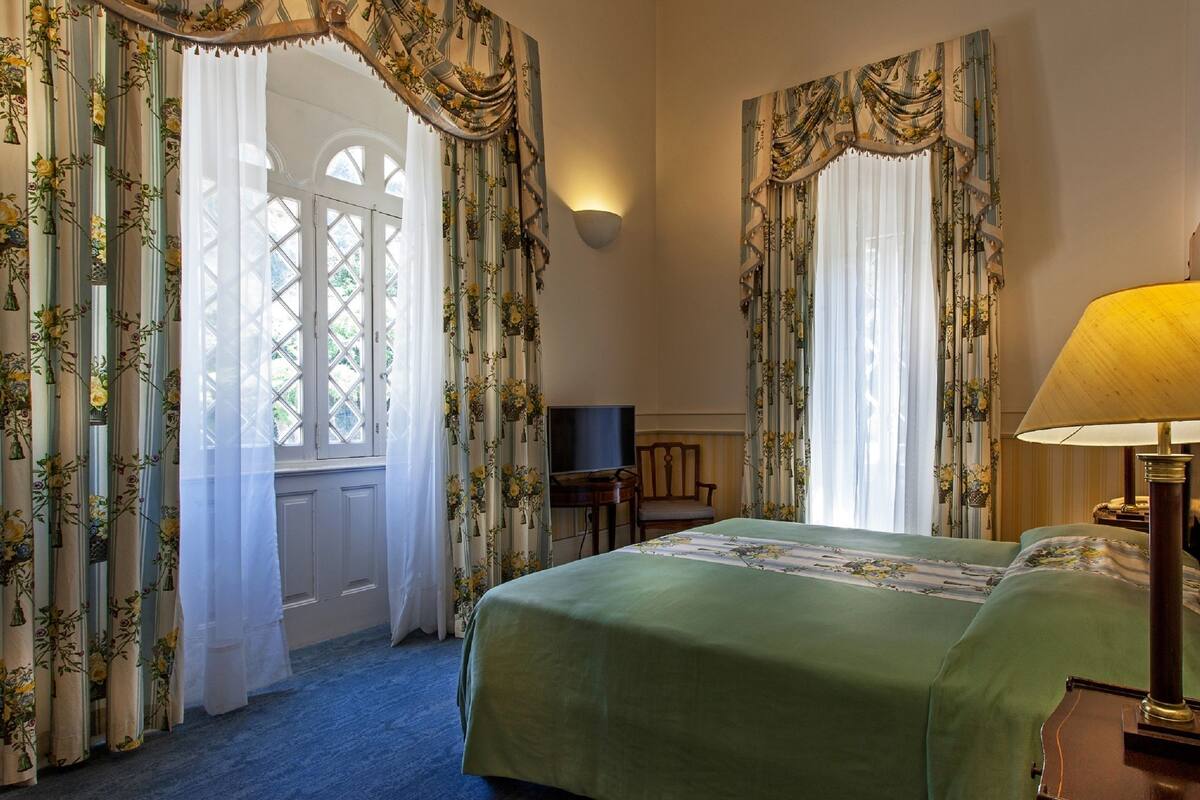 A hotel room with a bed, a desk with a television, and curtains with floral patterns.