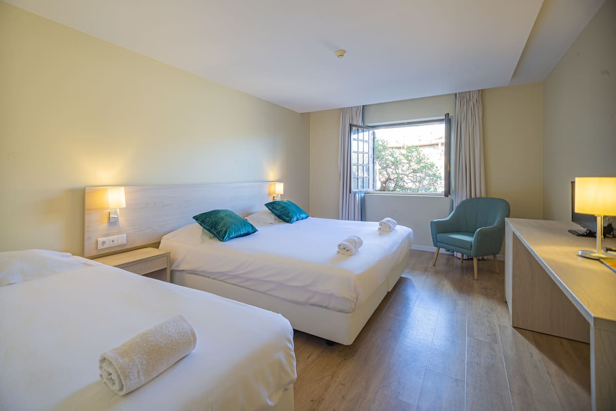 Une chambre d’hôtel avec deux lits, un bureau, une chaise et une fenêtre avec des rideaux.