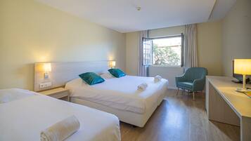 Habitación de hotel con dos camas, un escritorio, una silla y una ventana con cortinas.