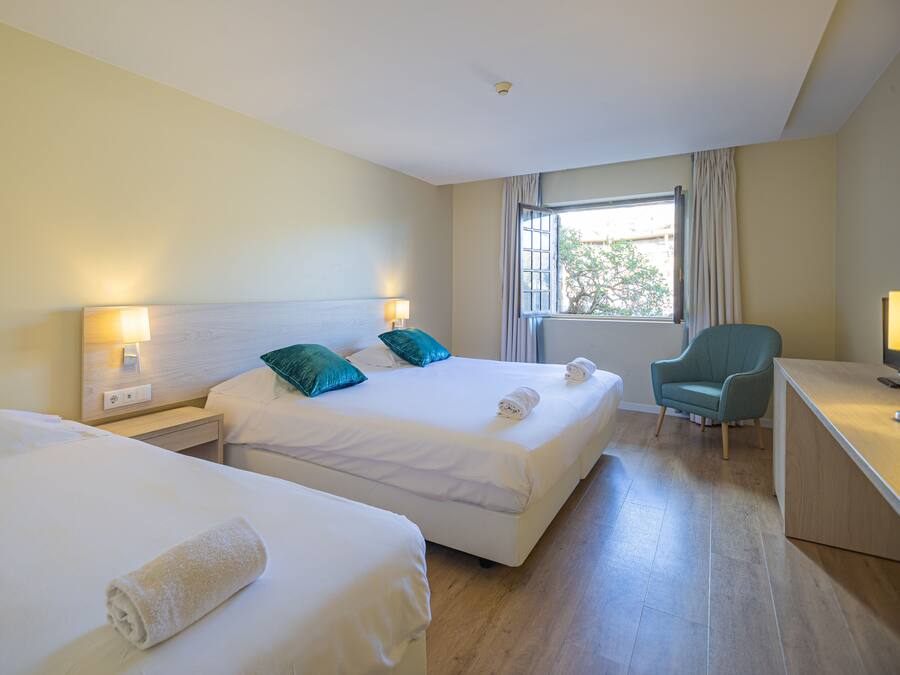 Habitación de hotel con dos camas, un escritorio, una silla y una ventana con cortinas.