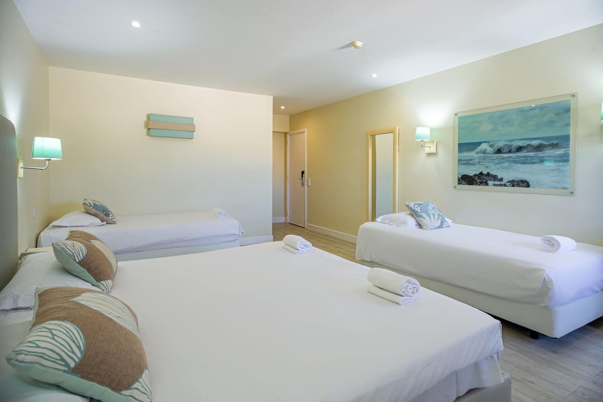 Une chambre d’hôtel avec deux lits simples, un grand tableau représentant l’océan et une porte donnant accès à la salle de bain.