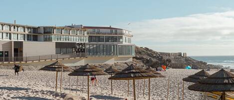 Ein Strand mit Sonnenschirmen, einem Gebäude und dem Meer.