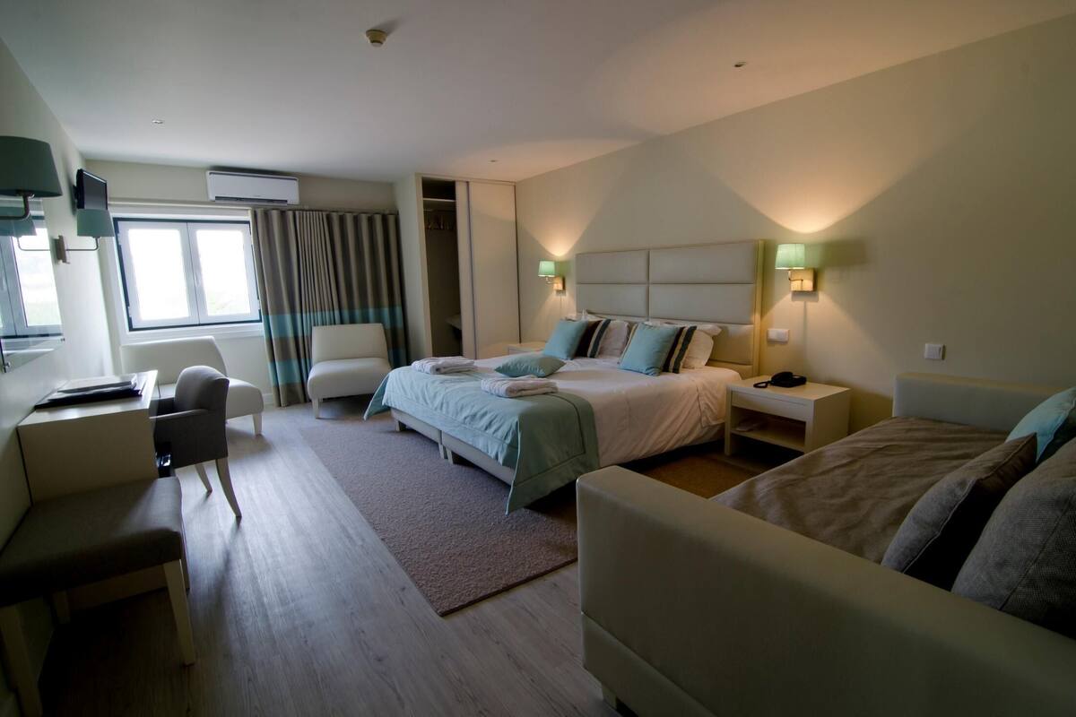 A hotel room with a bed, bedside tables, a desk, a chair, and a wardrobe.
