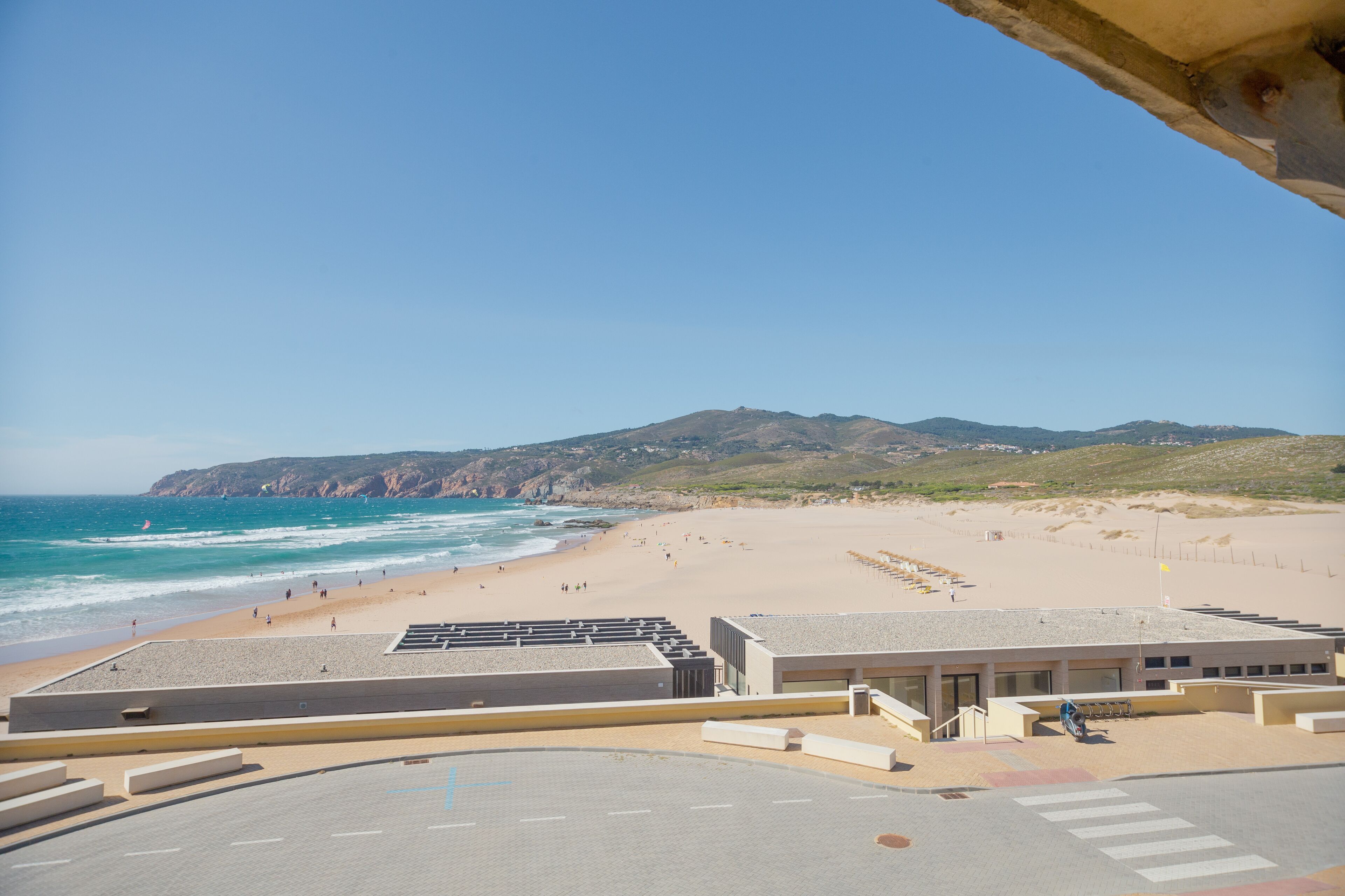 Une vue sur la plage avec un bâtiment au premier plan, une plage de sable et une montagne en arrière-plan.