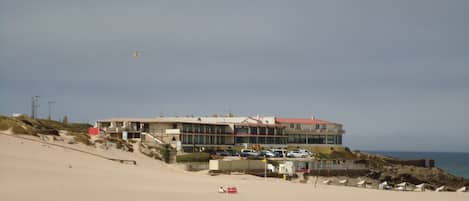 A beachfront property with a large building, a sandy beach, and a view of the ocean.