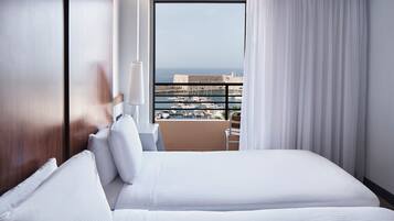 Habitación de hotel con una cama grande, una silla, un escritorio y vistas al mar y a las embarcaciones.