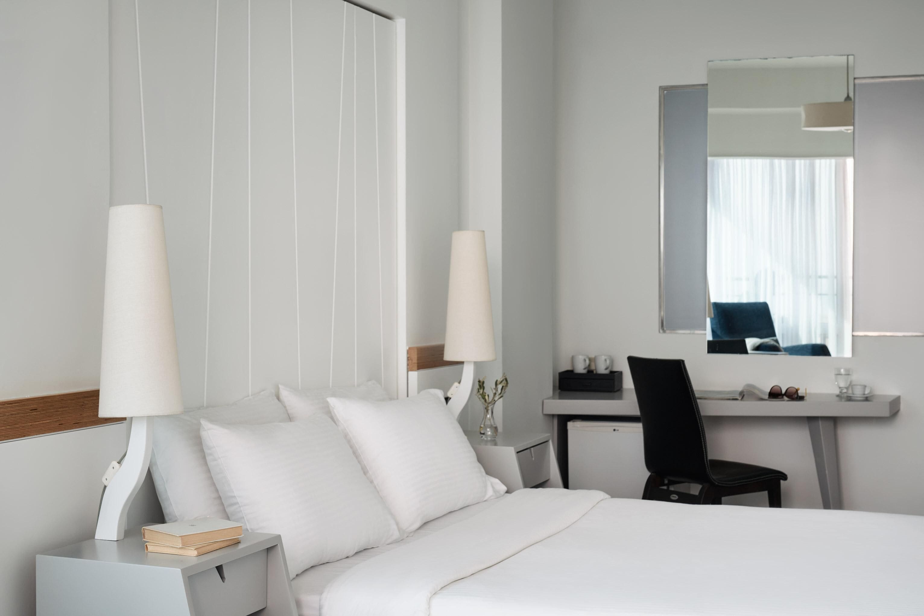 A hotel room with a bed, bedside tables, a desk, a chair, and a mirror.