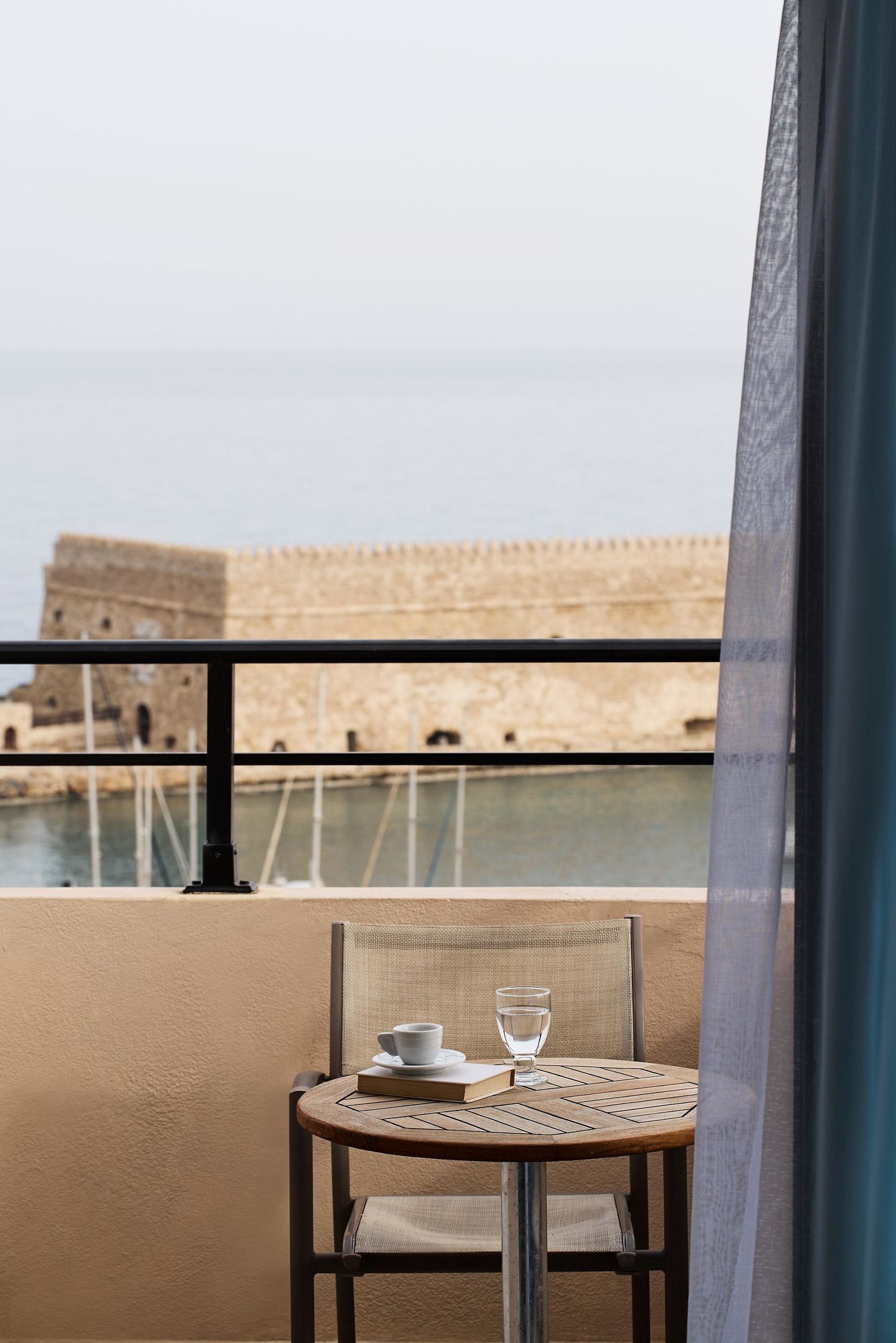 A balcony with a table set for two, overlooking a historic fort and a body of water.