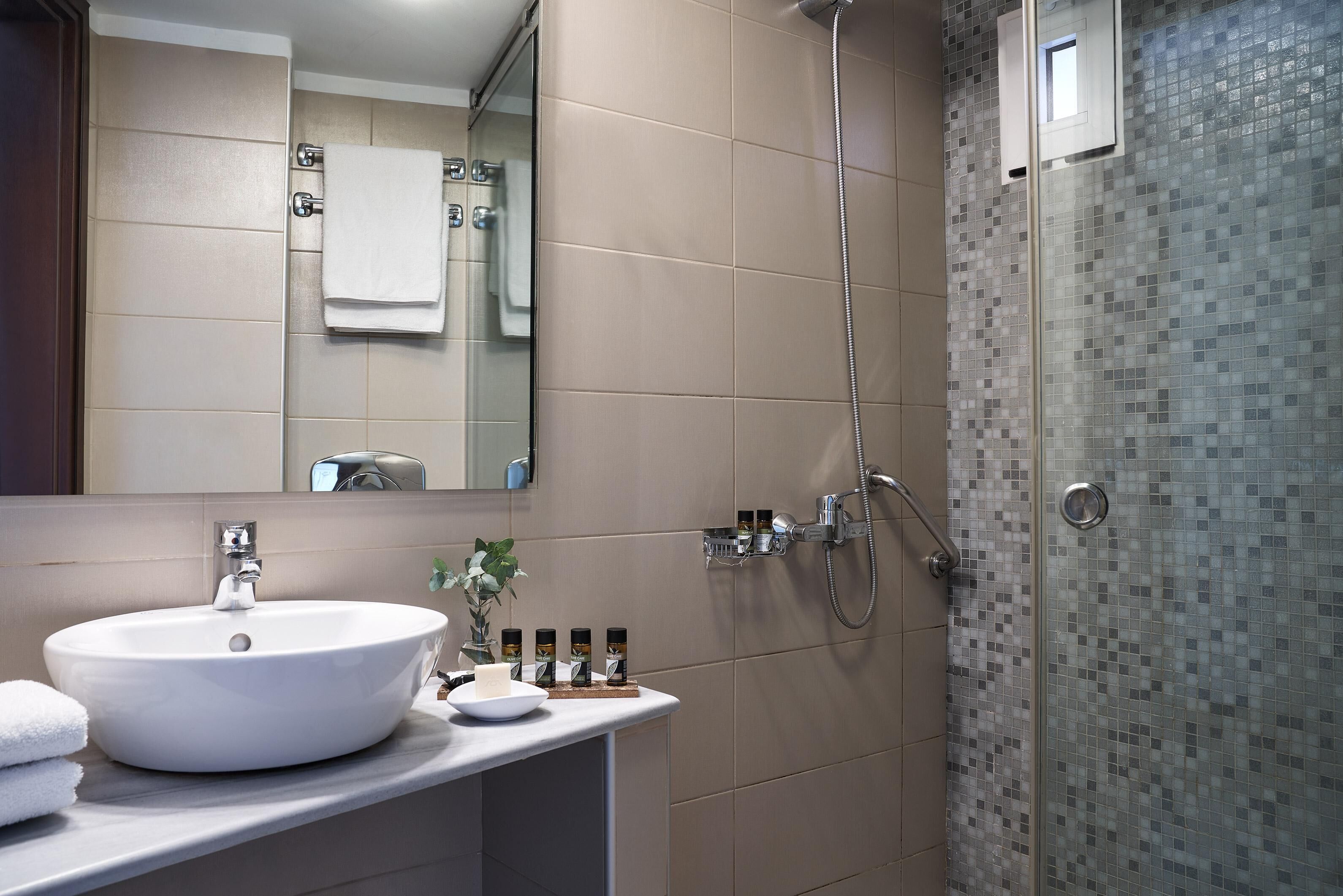 Un baño con un lavamanos grande de color blanco, un espejo, una ducha con puerta de vidrio y un revestimiento de azulejos.