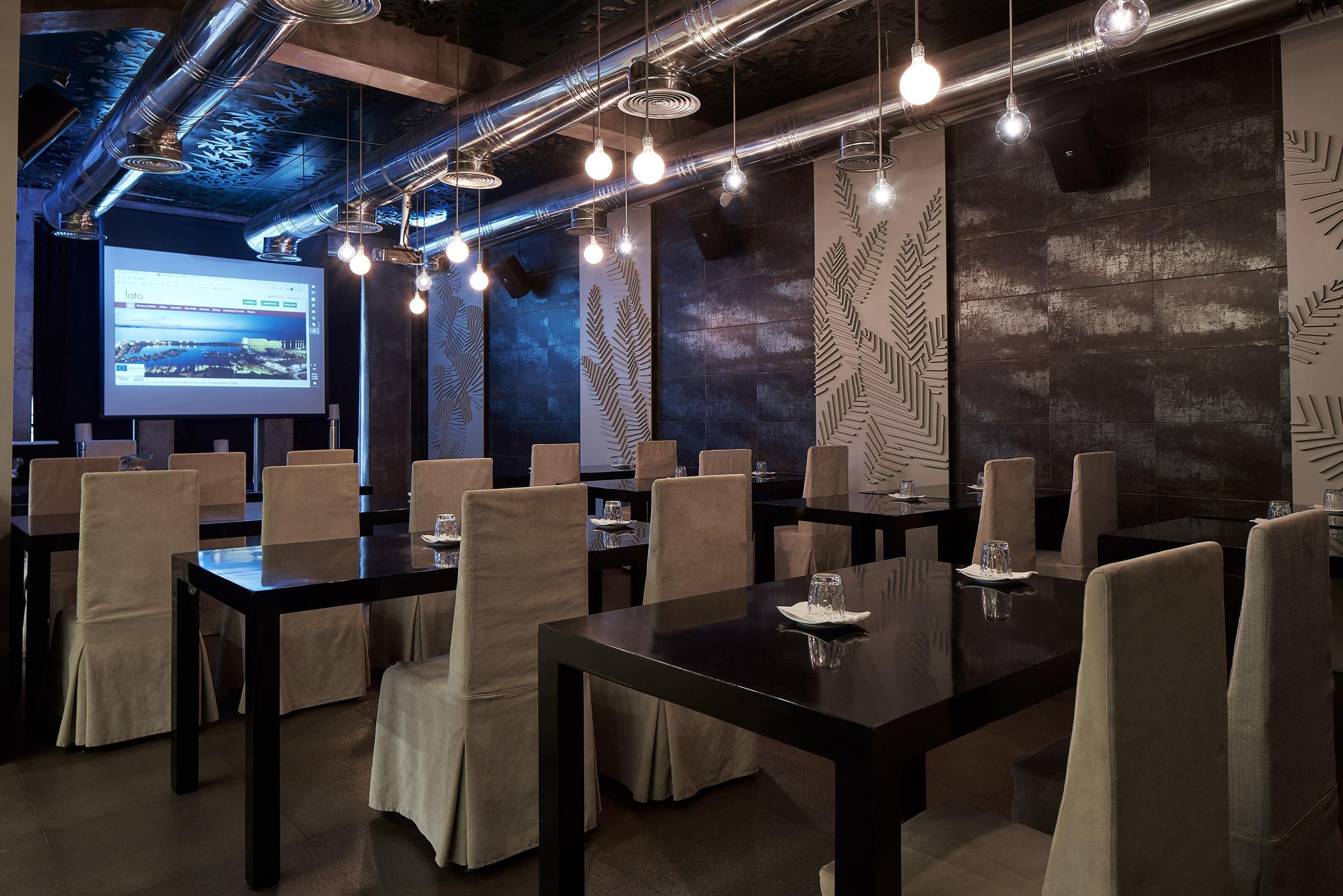 Un salón de conferencias con mesas y sillas, una pantalla de proyector y diseños de hojas decorativas en las paredes.