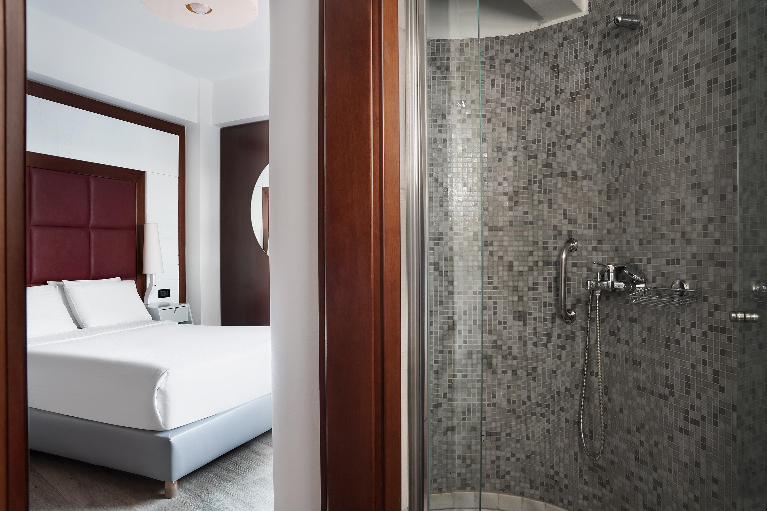 Ein modernes Hotelzimmer mit einem großen Bett, einer Dusche mit Mosaikfliesen und einem Holztürrahmen.