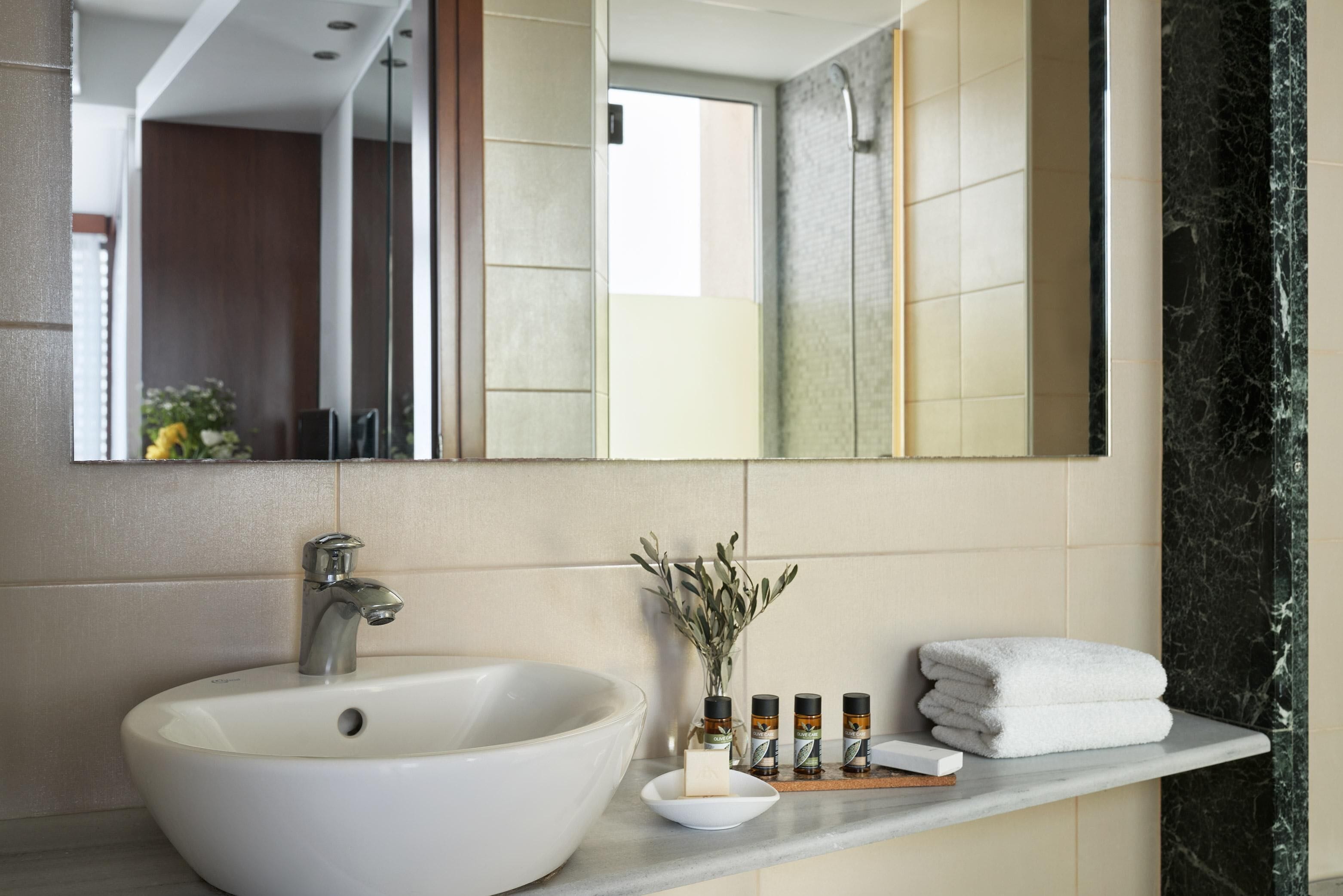 Een badkamer met een groot wit wastafelmeubel, een spiegel en een marmeren wand. Er staan toiletartikelen op het aanrecht.
