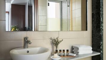 Een badkamer met een groot wit wastafelmeubel, een spiegel en een marmeren wand. Er staan toiletartikelen op het aanrecht.