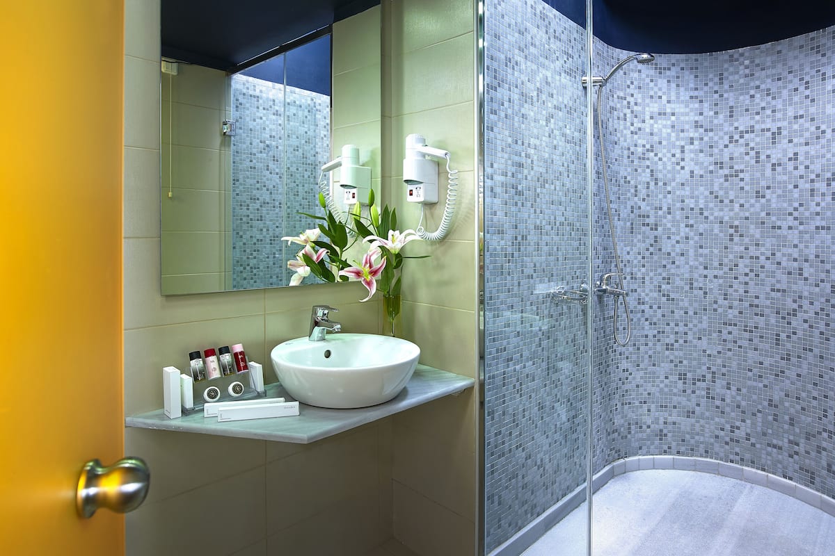 Un baño con lavamanos blanco, espejo, ducha con puerta de vidrio y pared de azulejos.