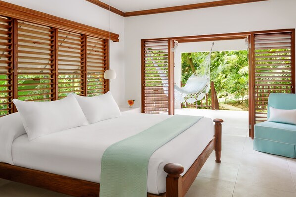 A bedroom with a large bed, wooden blinds, a hammock, and a view of greenery.