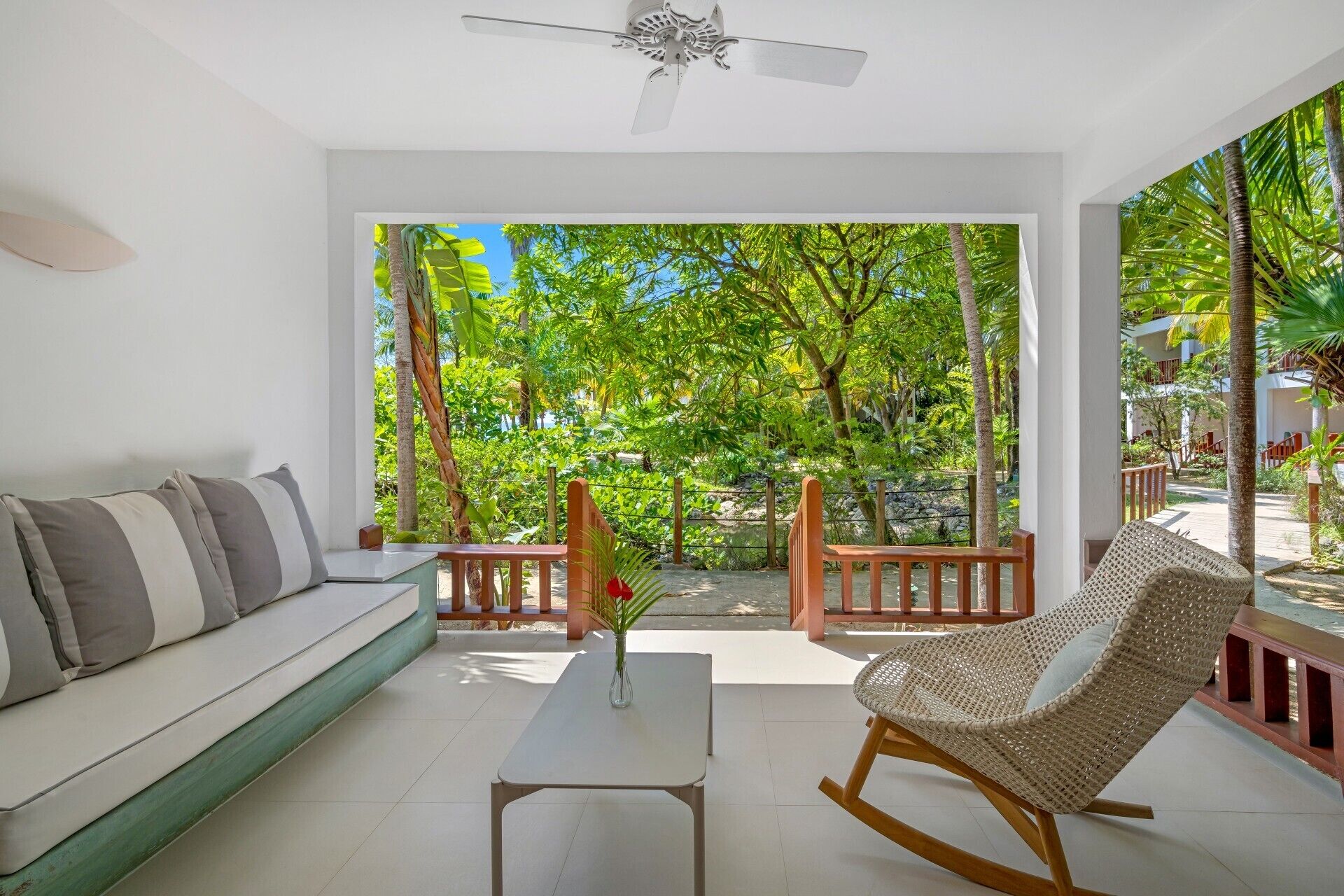 Una sala de estar moderna con un sofá, un sillón mecedor y una mesa de centro. Se ve un jardín exuberante a través de un ventanal.