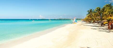 A beach with clear turquoise water, white sand, and palm trees.