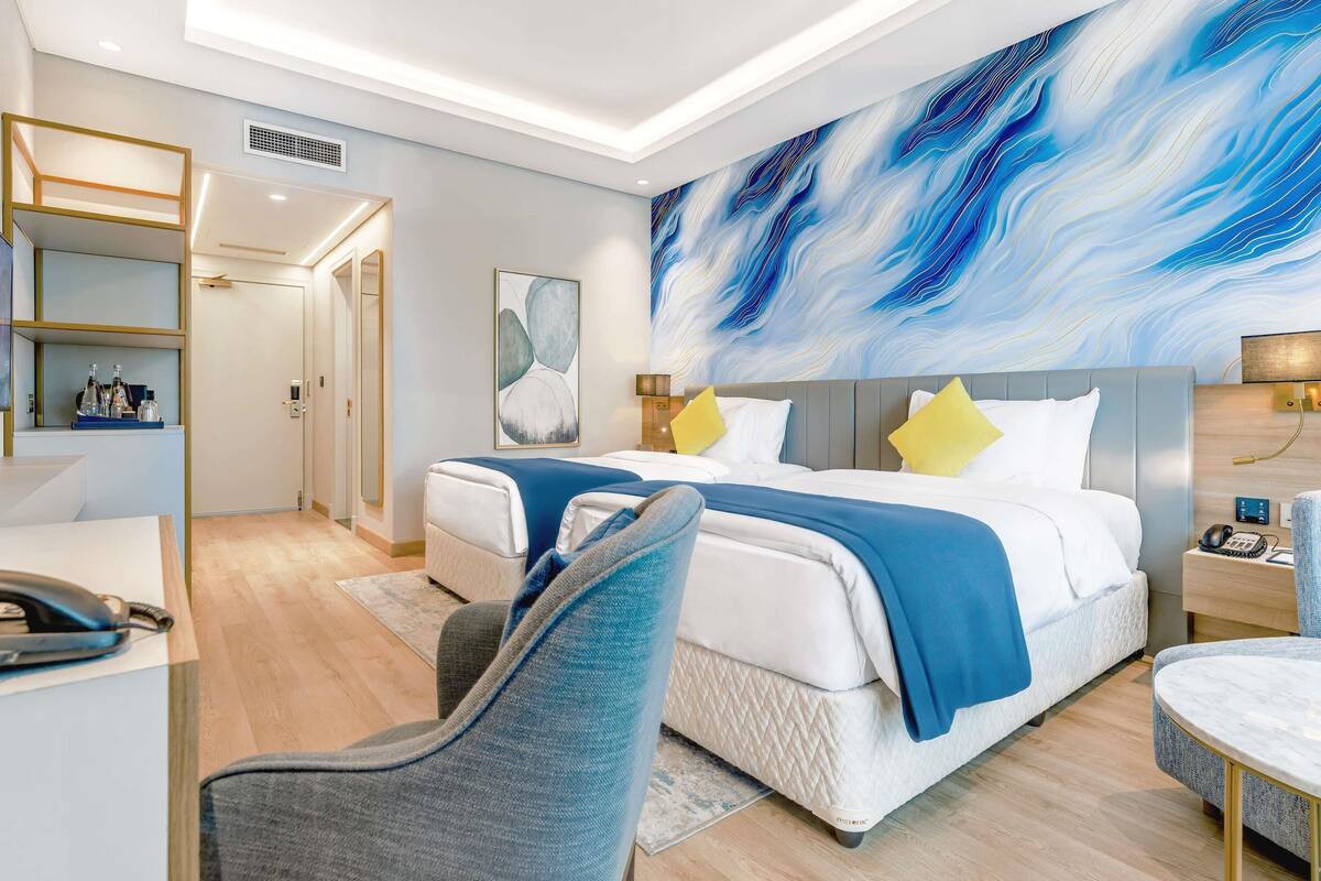 A modern hotel room with a large bed, bedside tables, a desk, and a chair.