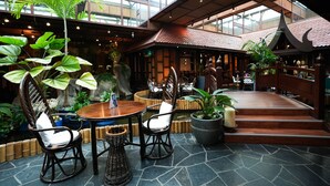 Un comedor interior con una mesa redonda, sillas de mimbre y una planta en maceta.