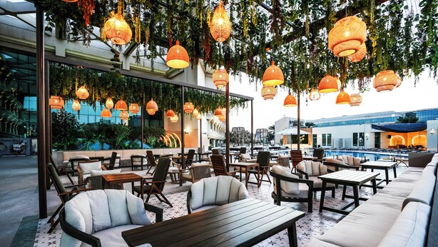 An outdoor seating area with tables and chairs, a pool in the background, and hanging lanterns.