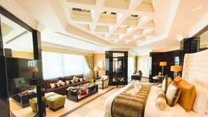 A spacious hotel room with a large bed, a sofa, a dining table, and a TV.