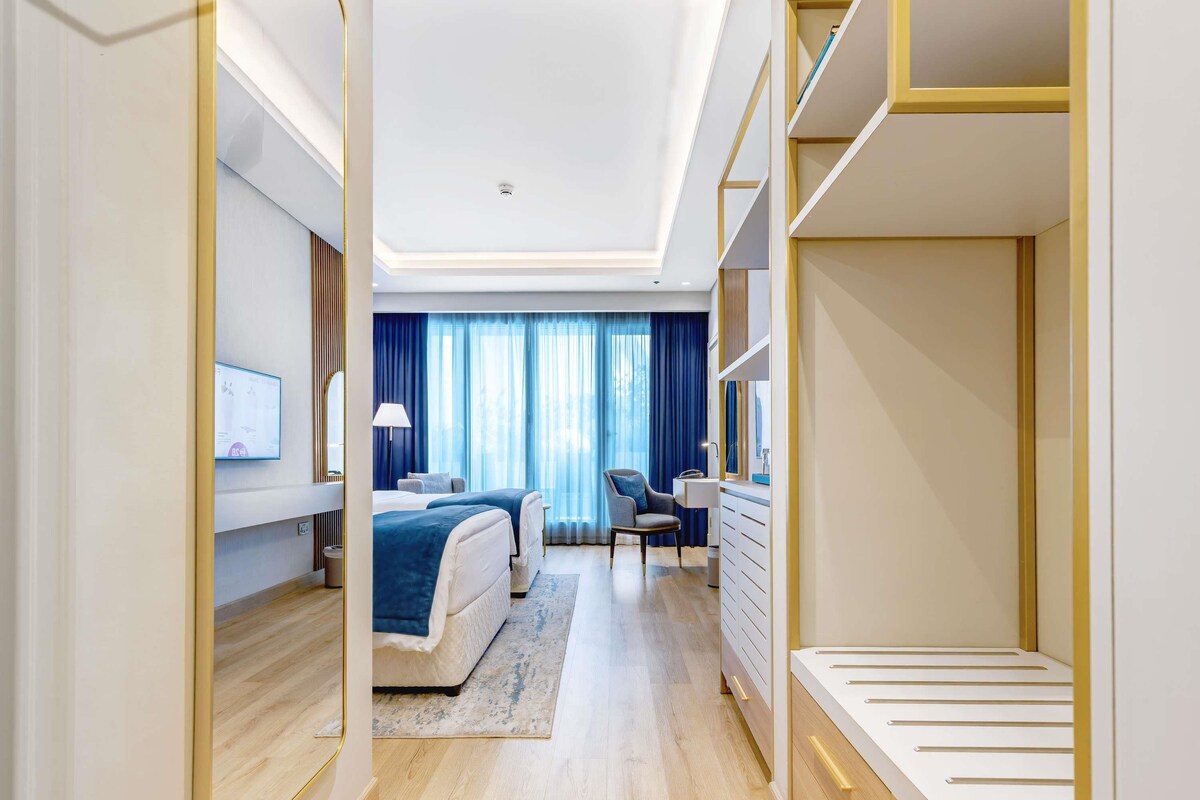 A modern hotel room with a bed, bedside table, lamp, and a desk with drawers.