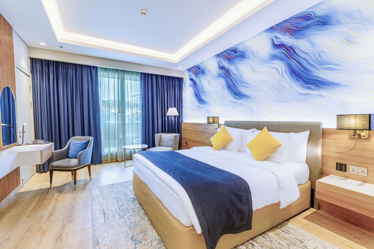 A modern hotel room with a large bed, a desk, a chair, and a wall with a blue abstract design.