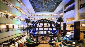 Un vestíbulo de hotel de varios niveles con un atrio central, palmeras y una zona de piscina.
