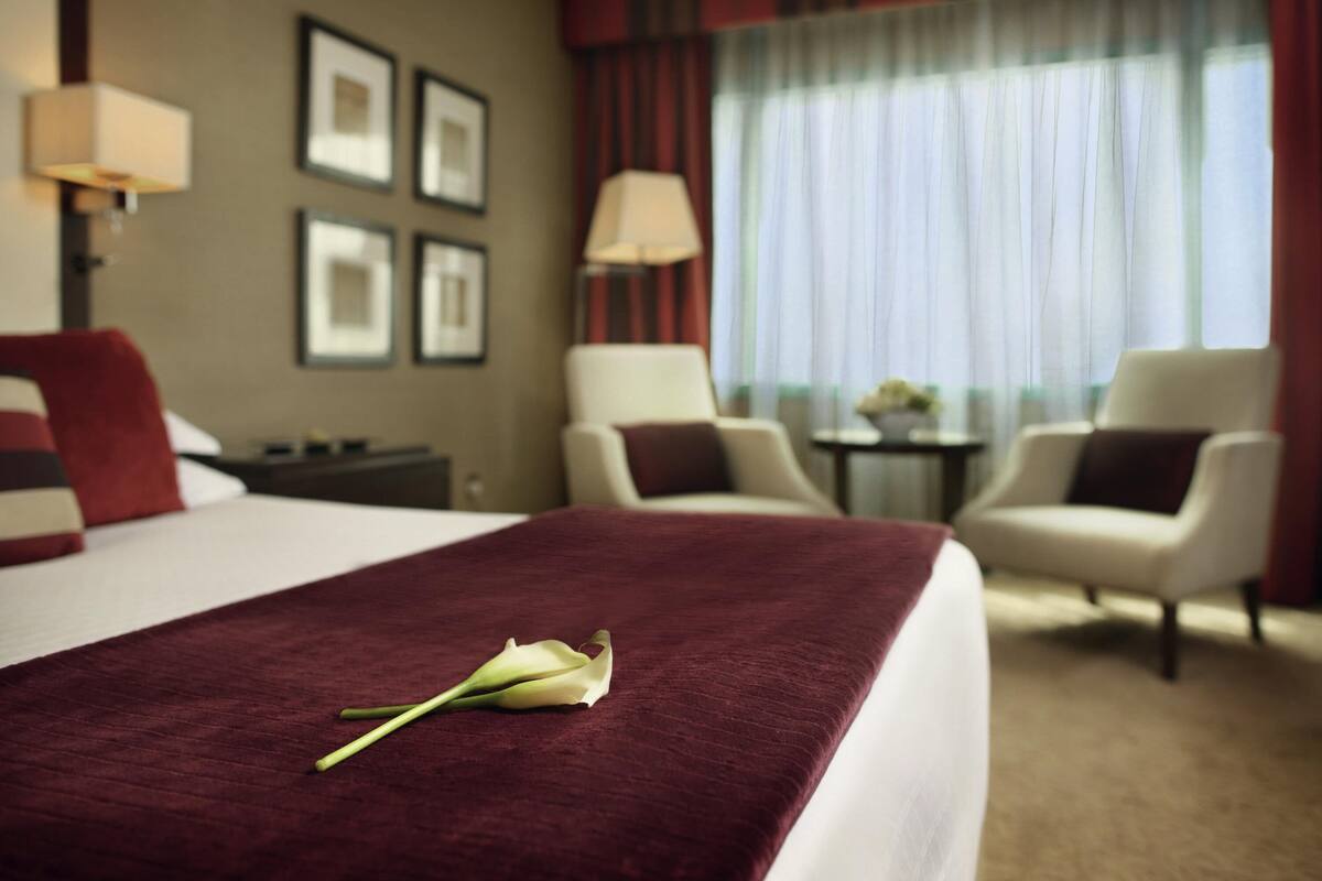 A hotel room with a bed, two armchairs, a small table, and a window with curtains.