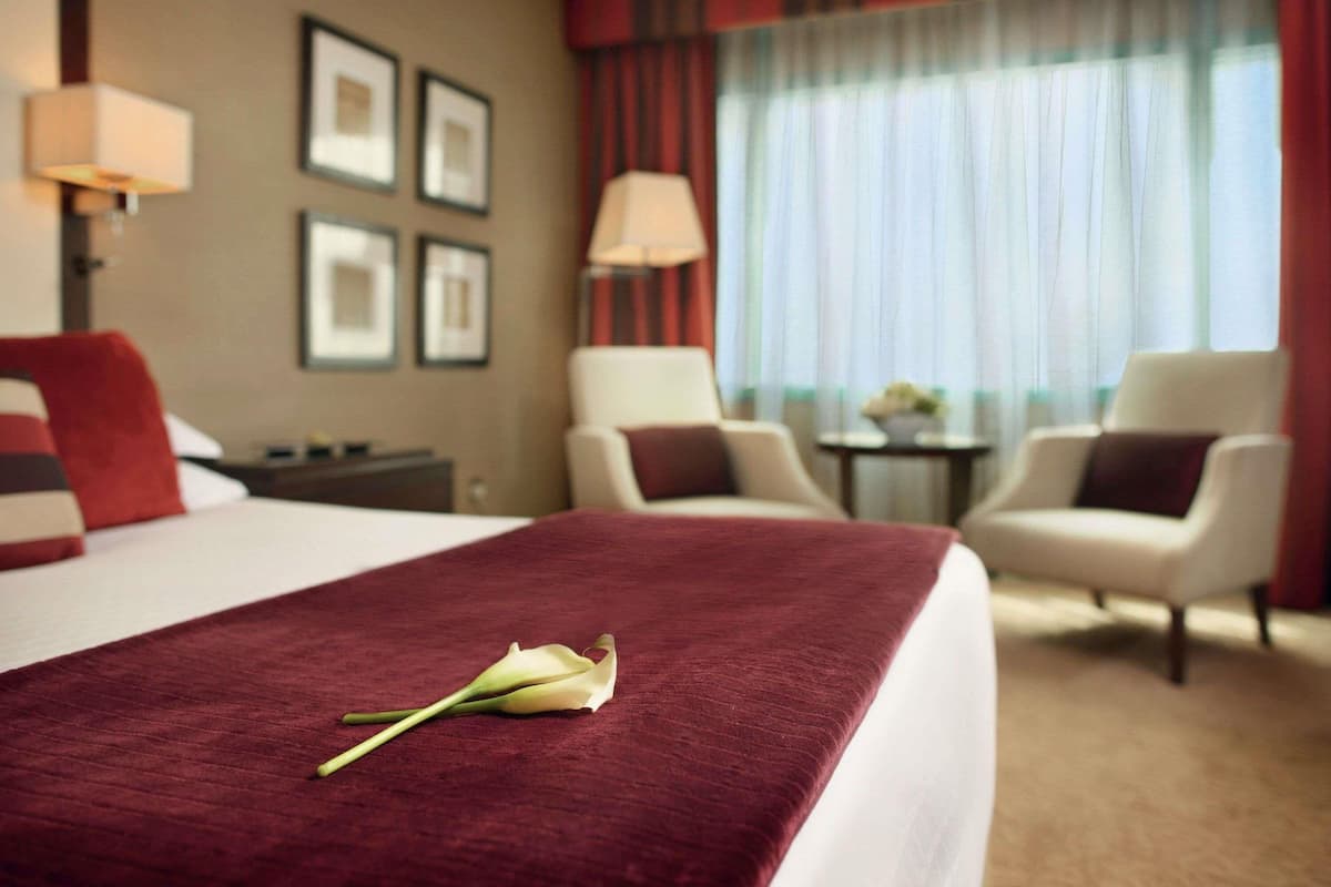 A hotel room with a bed, two chairs, a small table, and a window with curtains.