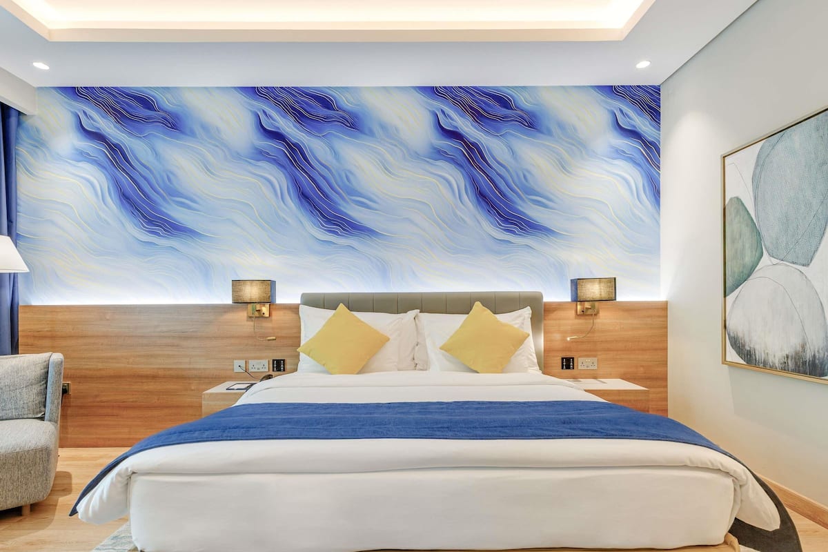 A modern hotel room with a large abstract mural, a neatly made bed, and a wooden headboard.