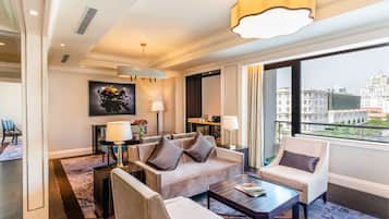 A modern hotel room with a sofa, armchairs, a coffee table, and a large window offering a city view.