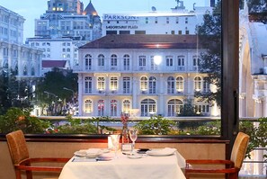 Ein Esstisch gedeckt mit Tellern, Gläsern und einer Vase, mit Blick auf eine Stadtlandschaft mit historischen Gebäuden.
