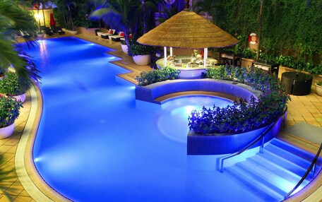 A swimming pool with a bar area, surrounded by potted plants and a thatched-roof structure.