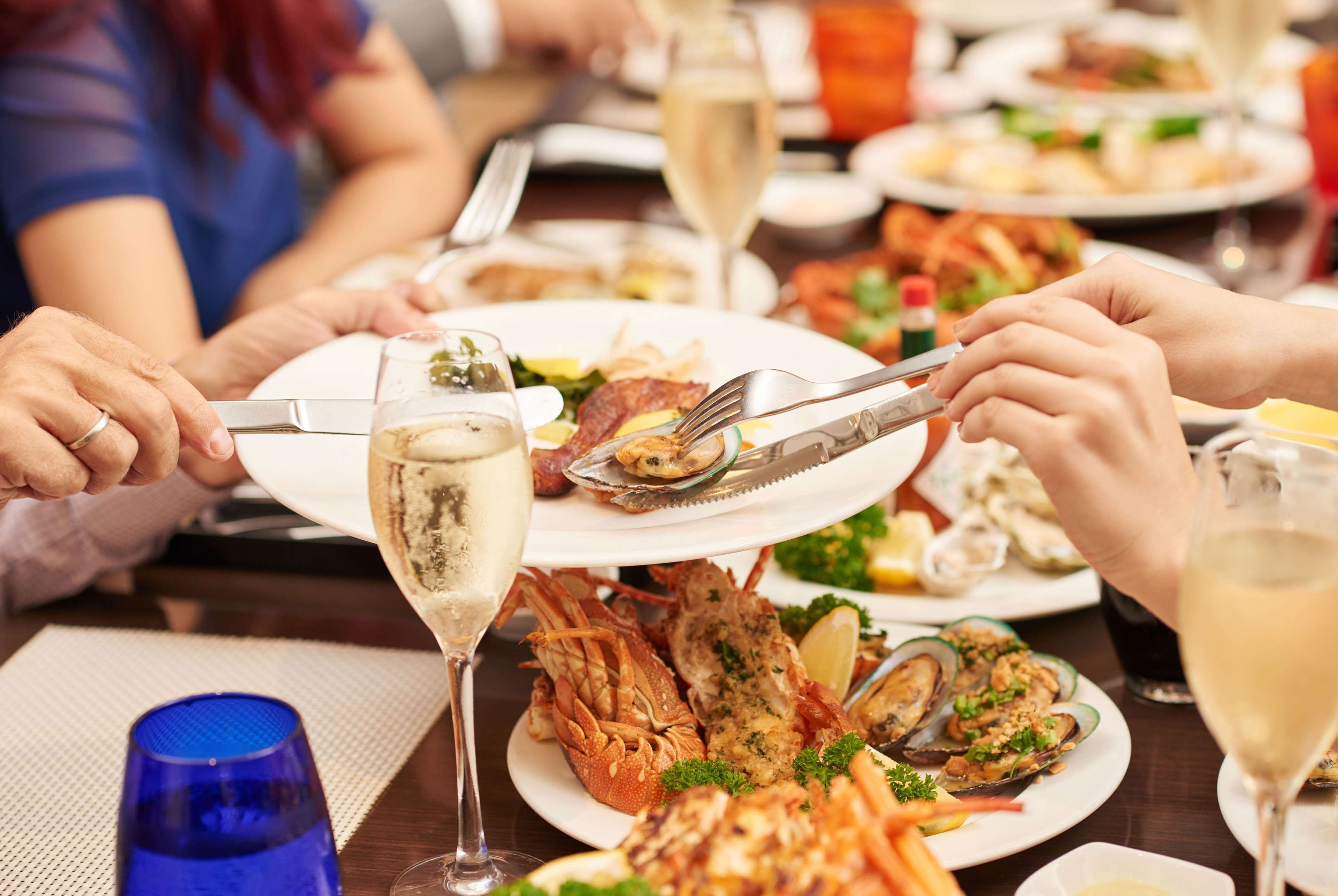 A dining table with seafood dishes, wine glasses, and people dining.