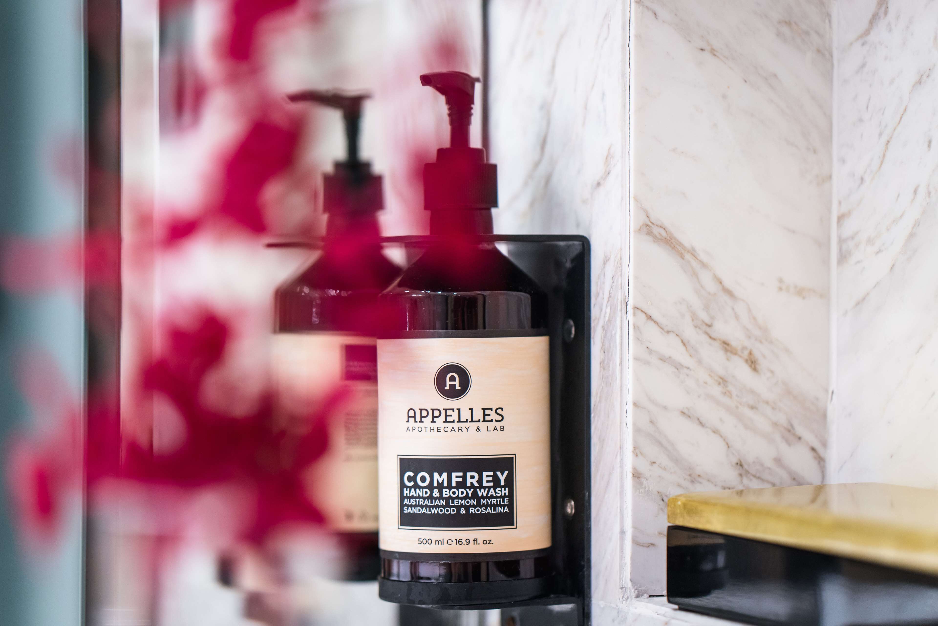 A bathroom with a marble wall, a black soap dispenser, and a gold-colored counter.