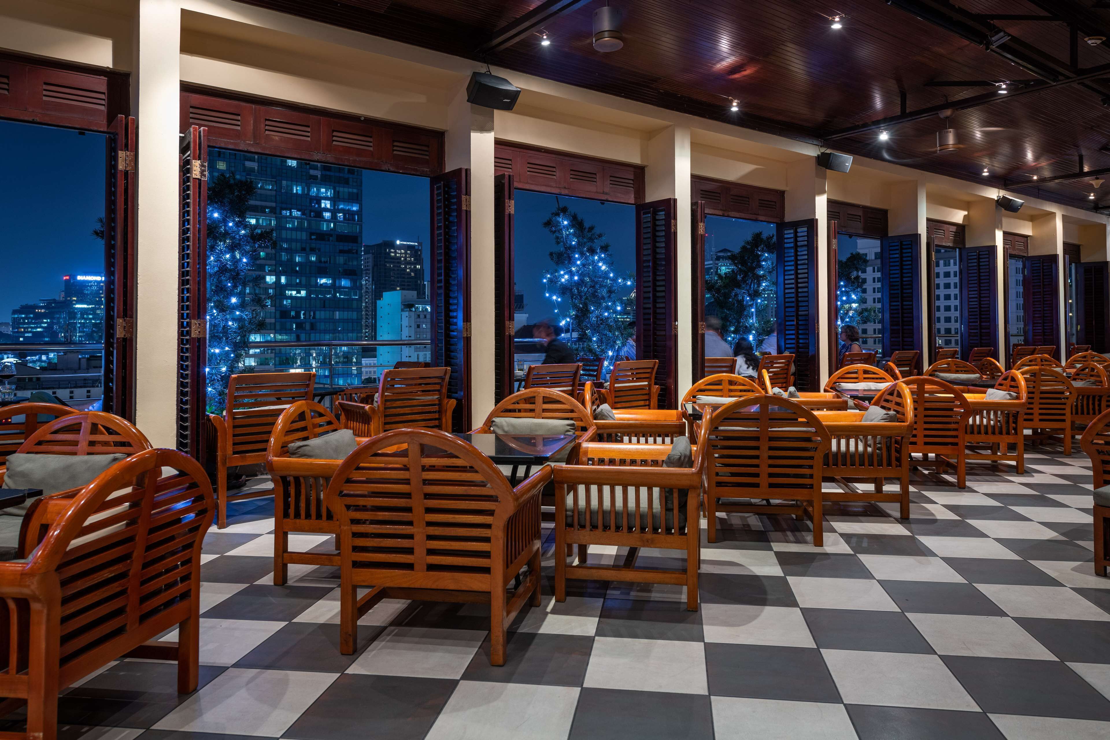 Un restaurante con sillas y mesas de madera, amplias ventanas con vistas a la ciudad y suelo a cuadros.