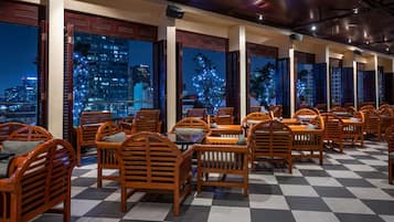 Un restaurante con sillas y mesas de madera, amplias ventanas con vistas a la ciudad y suelo a cuadros.