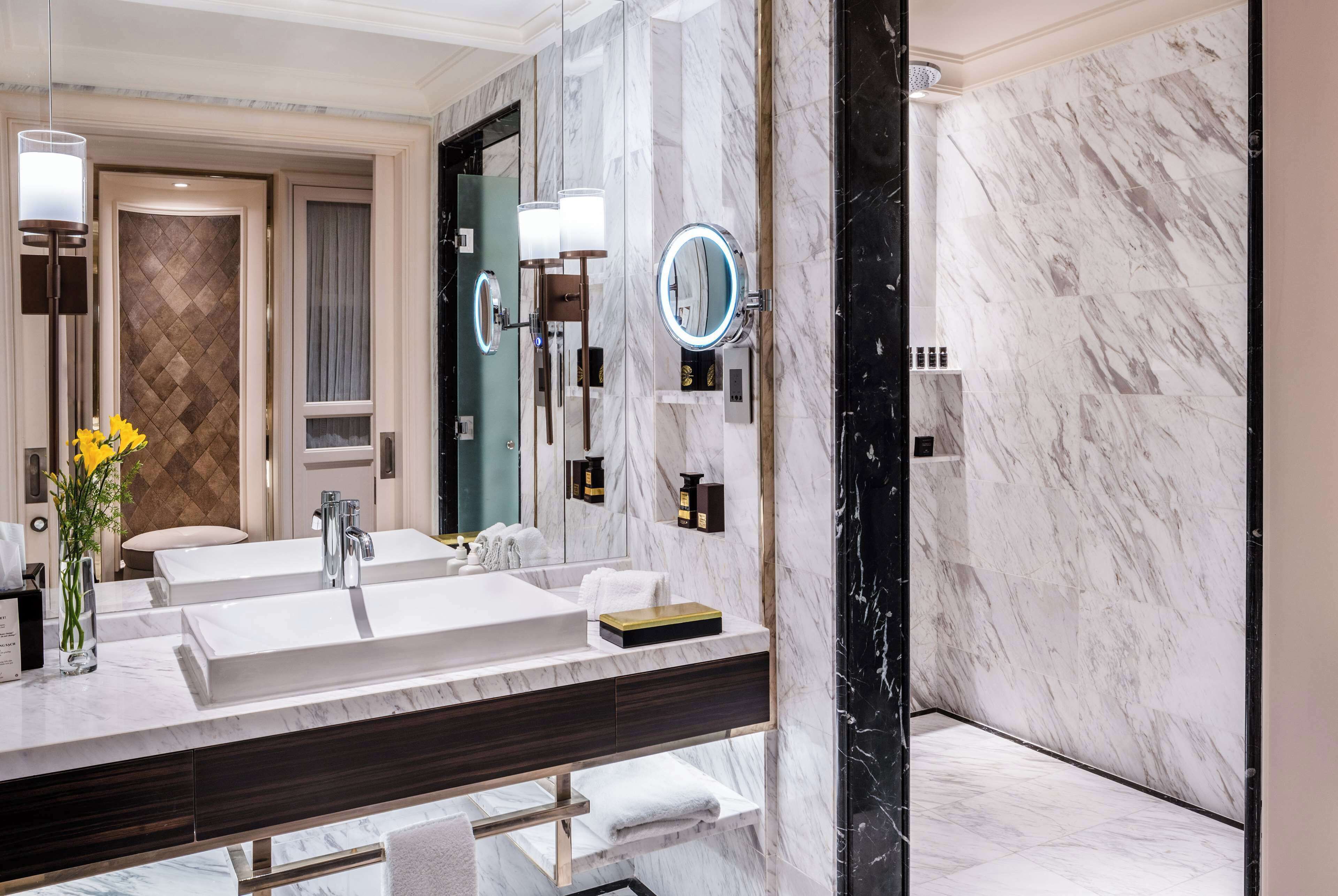 A modern bathroom with a large mirror, two sinks, and a marble wall.