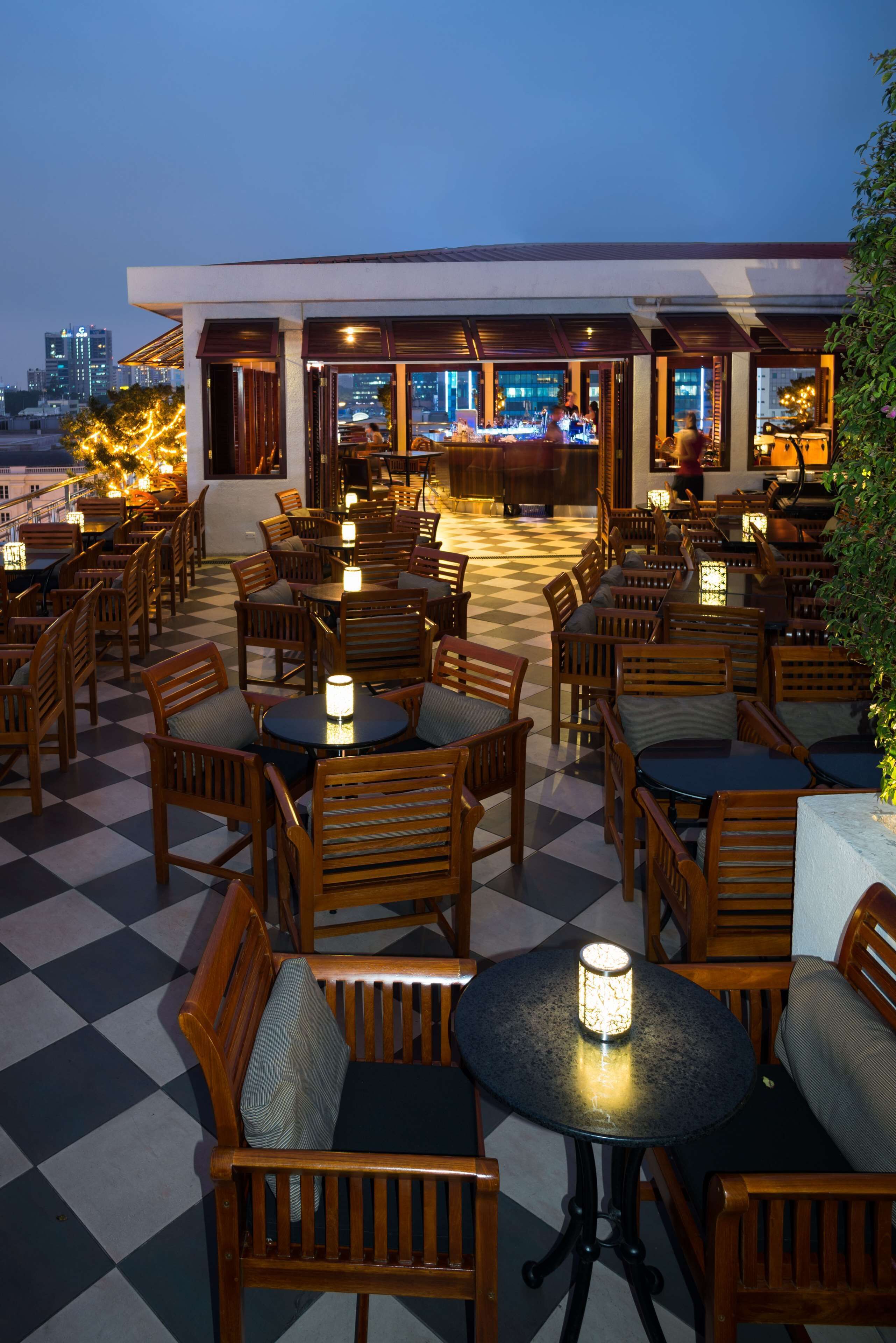 A rooftop restaurant with outdoor seating, a checkered floor, and a view of the city skyline.