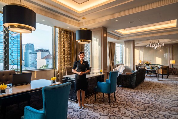 A hotel room with a desk, chairs, a sofa, a dining area, and a view of the cityscape.