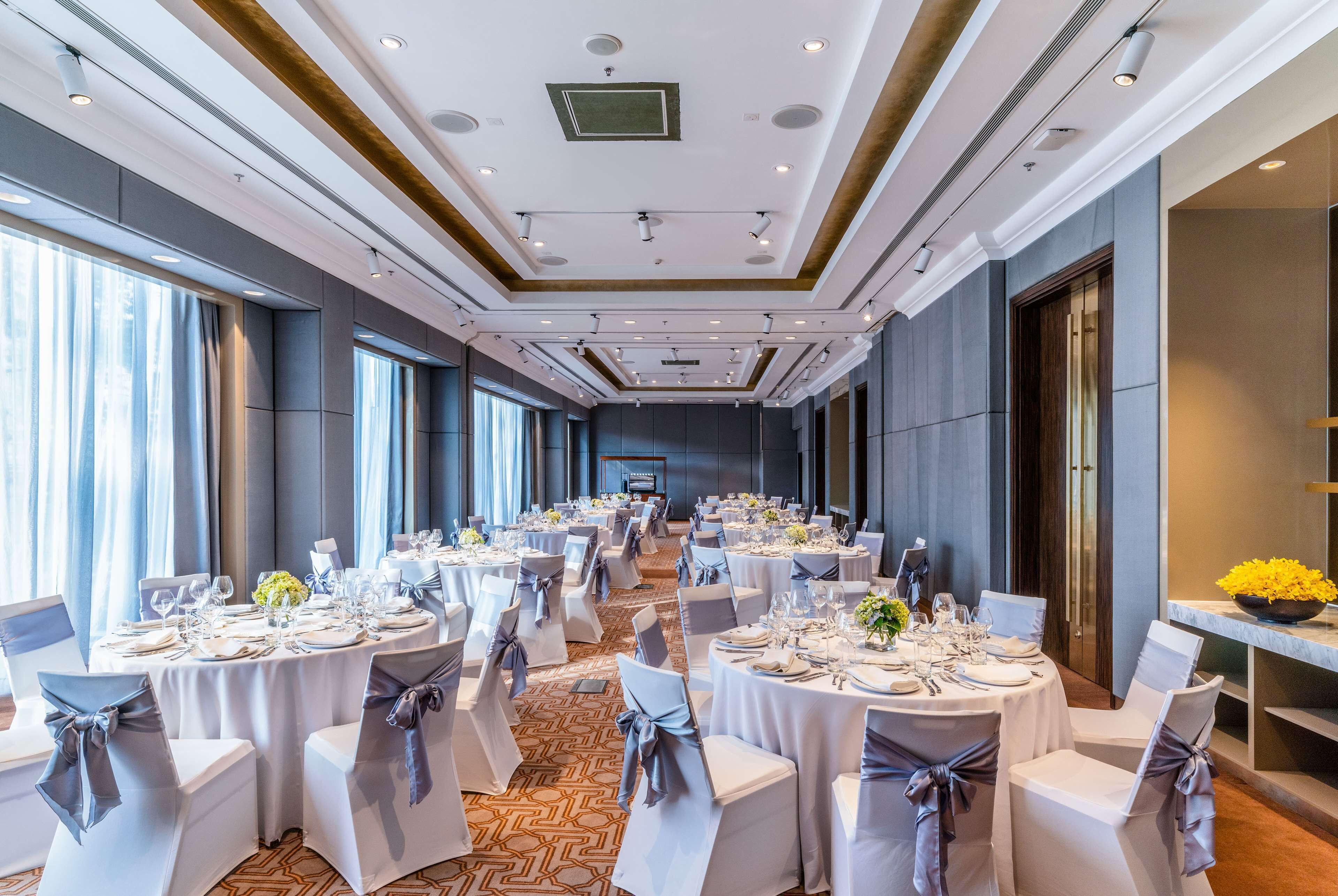Un salón de banquetes con mesas redondas, sillas y una mesa larga con un escenario al final.