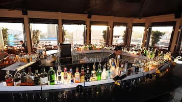 Un bar avec un grand choix de bouteilles d’alcool, un barman et de grandes fenêtres donnant sur la ville.