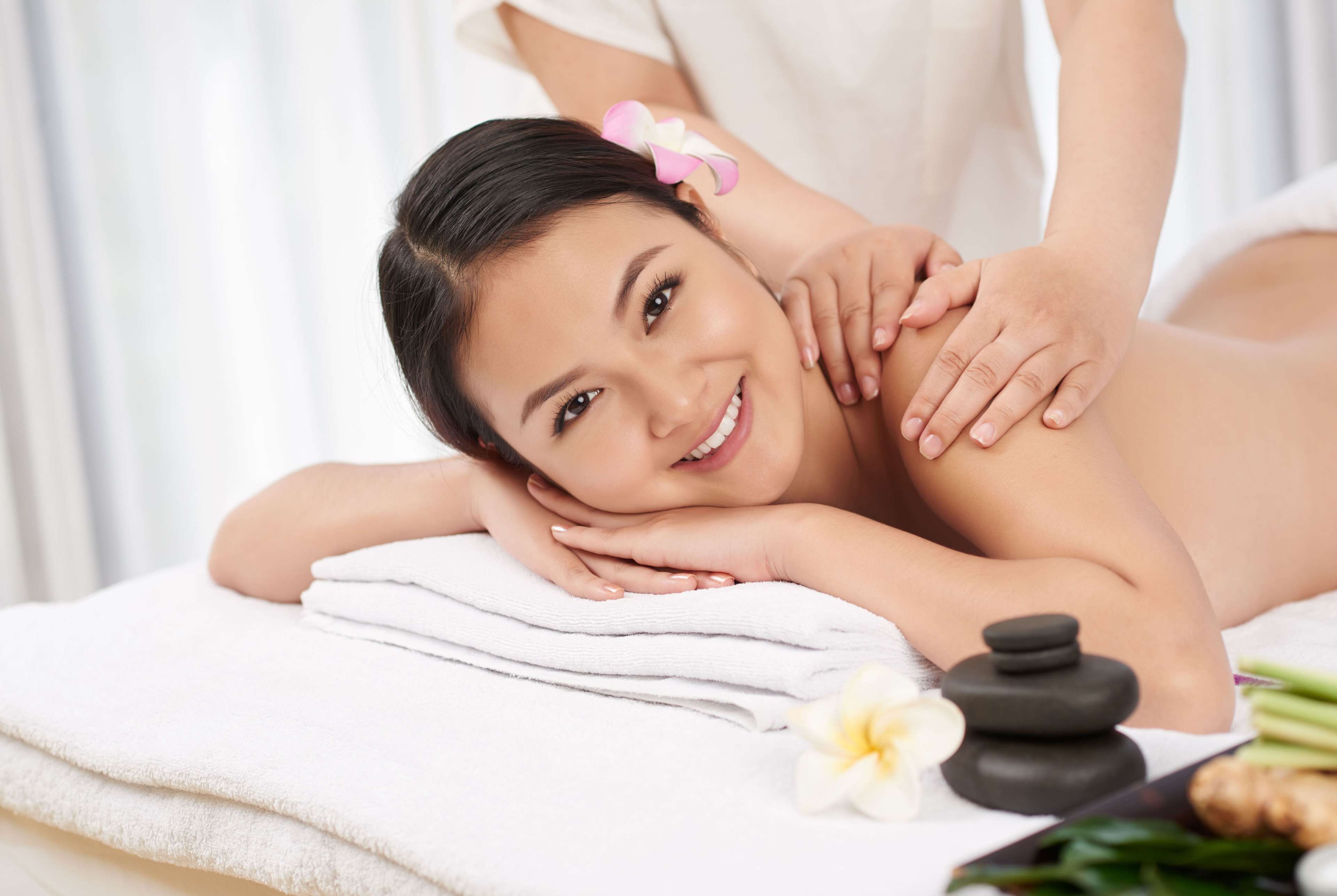 A person receiving a massage with a towel, a stone, and a flower on a massage table.