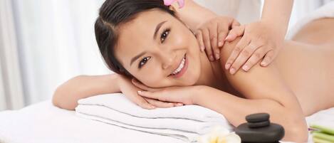 A person receiving a massage with a towel, a stone, and a flower on a massage table.