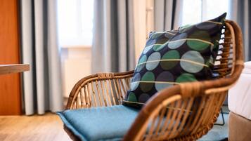 Une chaise en osier avec un coussin et un oreiller à pois, dans une pièce dotée d’une fenêtre et de rideaux.