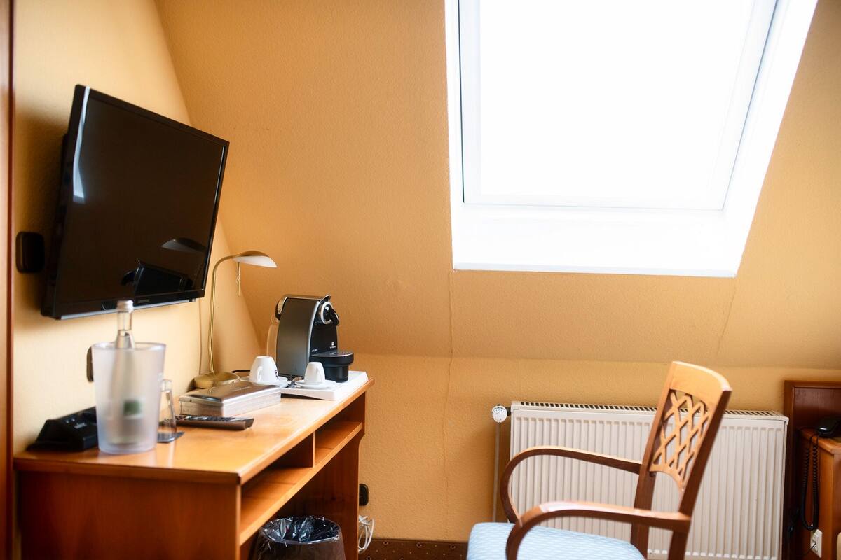 Une petite pièce agréable, dotée d’un bureau, d’une chaise, d’un téléviseur, d’une machine à café et d’un radiateur.