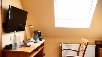 A small, cozy room with a desk, a chair, a television, a coffee machine, and a radiator.