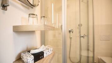 Un bagno con box doccia in vetro, uno scaffale in legno con un portarozzi e uno specchio sopra lo scaffale.